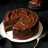 Chocolate cake with a slice removed on a white plate against a dark background