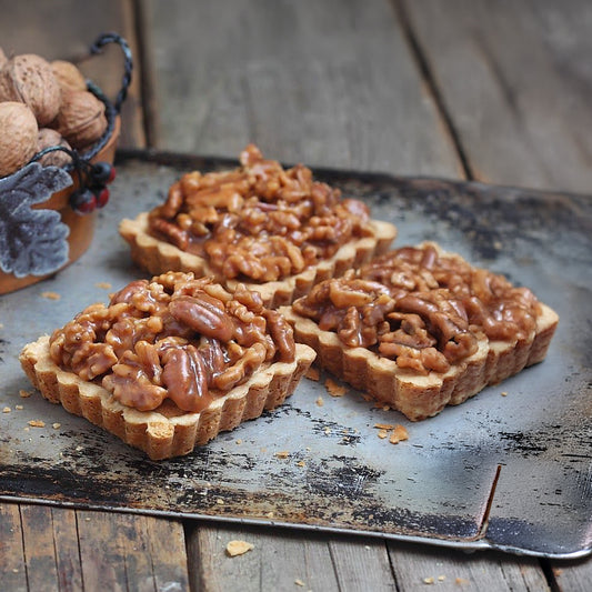 Three walnut tarts on a rustic metal tray with a wooden background