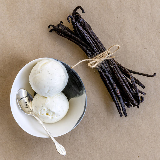Two scoops of vanilla ice cream in a bowl with a bundle of vanilla beans on a brown background. Desserts