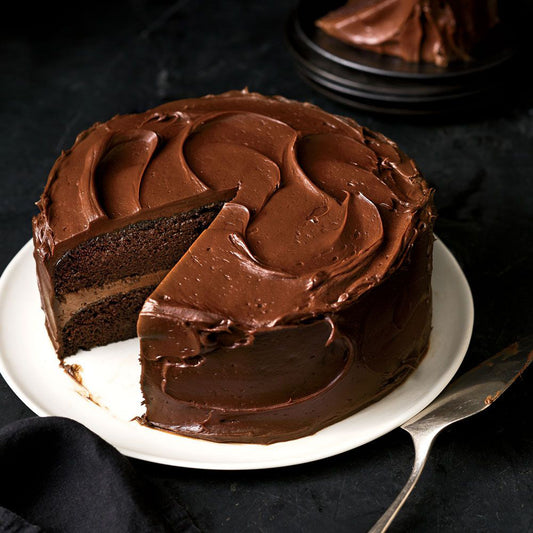 Chocolate cake with a slice removed on a white plate against a dark background