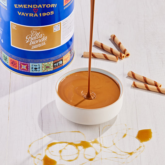 EVS09020_Salted_Caramel_Gourmet_Variegato_for_Gelato_Pastry_6kg_Bella_Bionda Bowl of caramel sauce with a bottle labeled 'Emendatori Vayra 1905' on a white surface.