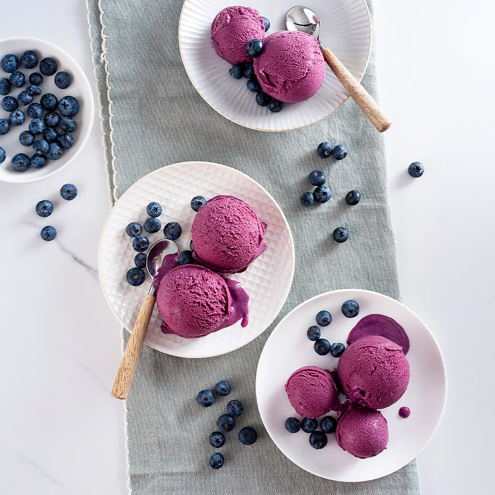 EVS10061_Blueberry_Flavour_Paste_for_Gelato_3.5kg_Pasta_Mirtillo Purple ice cream scoops on white plates with blueberries on a light gray cloth.