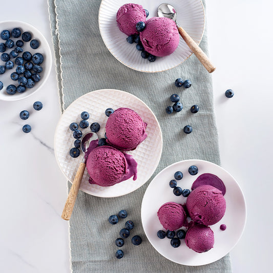EVS10061_Blueberry_Flavour_Paste_for_Gelato_3.5kg_Pasta_Mirtillo Purple ice cream scoops on white plates with blueberries on a light gray cloth.