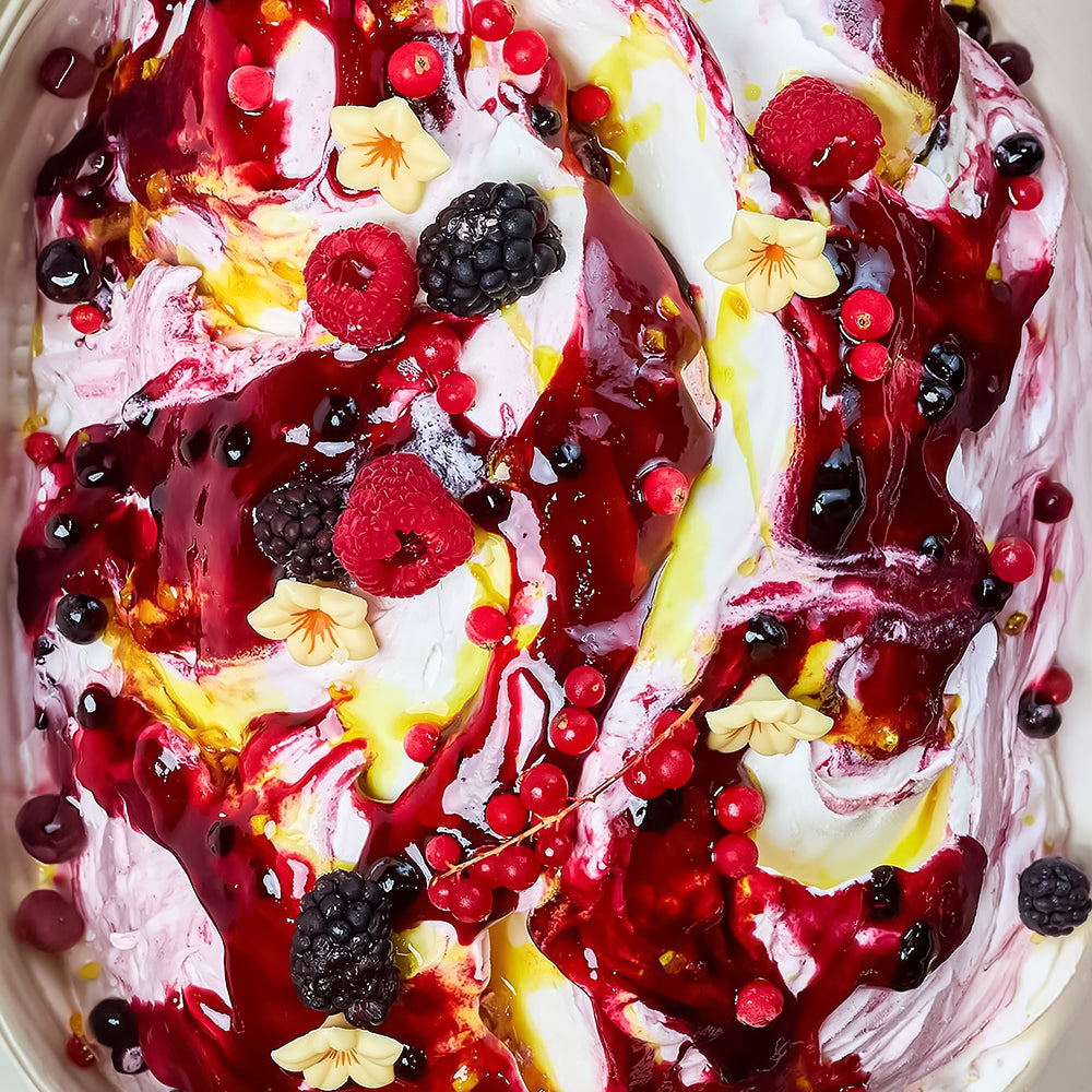 Dessert with ice cream, berries, and floral elements on a white plate