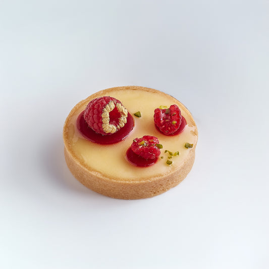 Small tart with raspberries and a gold leaf on a white background