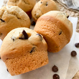 Chocolate chip muffins on a marble surface with scattered chocolate chips.
