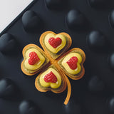 Four-leaf clover-shaped cookies with heart-shaped raspberries on a black background