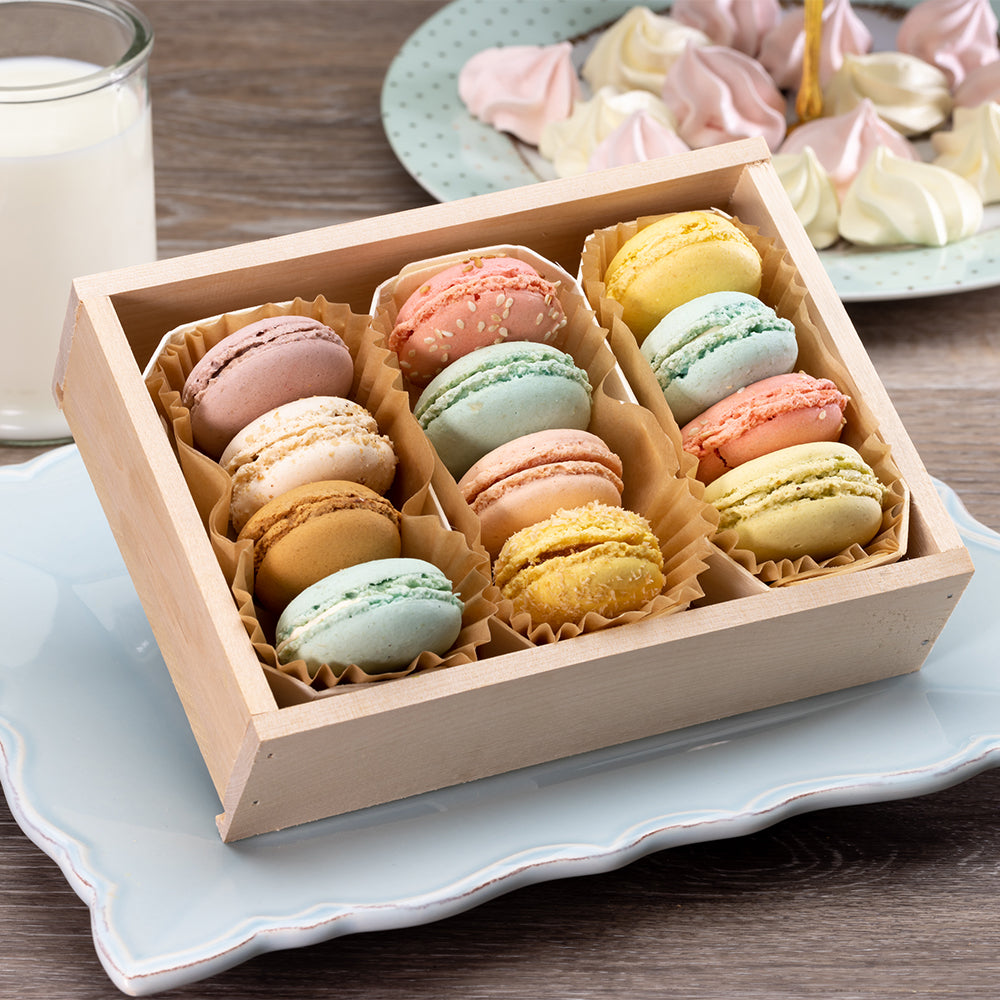 Box of colorful macarons on a light blue plate with a glass of milk.