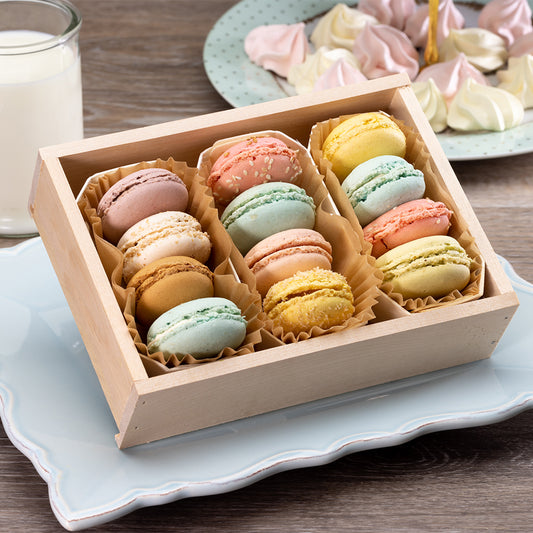 Box of colorful macarons on a light blue plate with a glass of milk.